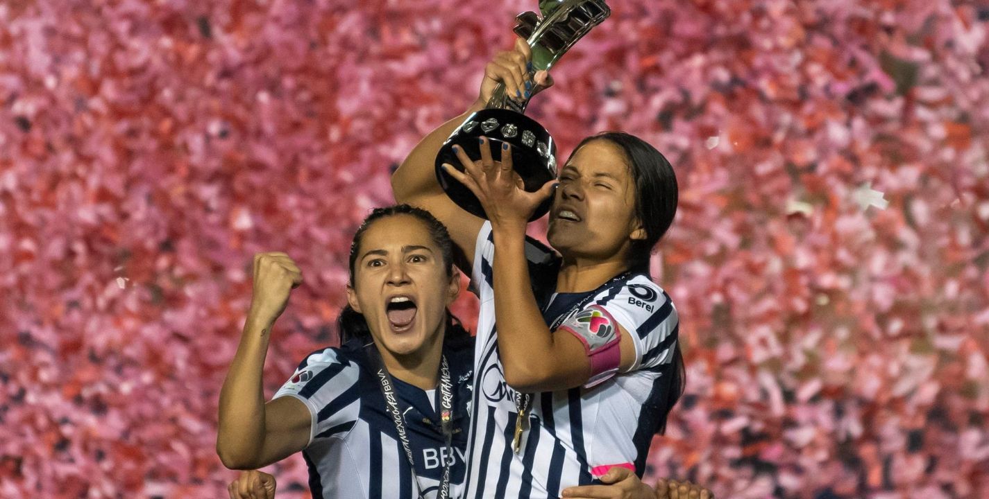 Desire Monsivais (i) y Rebeca Bernal (d) de Rayadas de Monterrey posan con el trofeo de campeonas luego de vencer a Tigres.